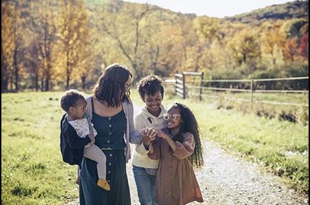 Mother with three children walking on a path with pastures on either side and a backdrop of trees.