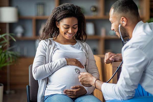 Pregnant black woman and male black doctor in doctors office listening to babys heart beat