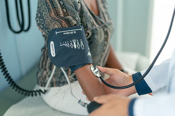 A mature adult woman of African descent is at a routine medical check. She is sitting on an examination table in a clinic. The nurse is using a blood pressure gauge to check the patient's blood pressure.