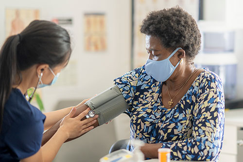 Medical worker checking a woman's blood pressure, both wearing masks