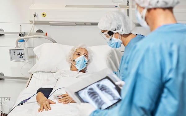 Medical professionals examining elderly woman patient in ICU on hospital bed. El