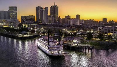 Photo of New Orleans at sunset, with a paddle boat on the Mississippi River in the foreground.