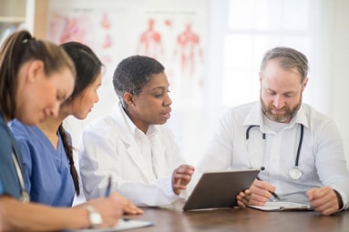 A team of four medical professionals reviewing records around a table.