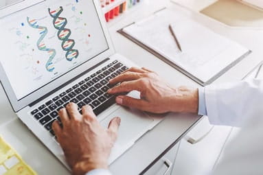 A close-up view of a white male scientist working on a laptop with diagrams of DNA on the screen.