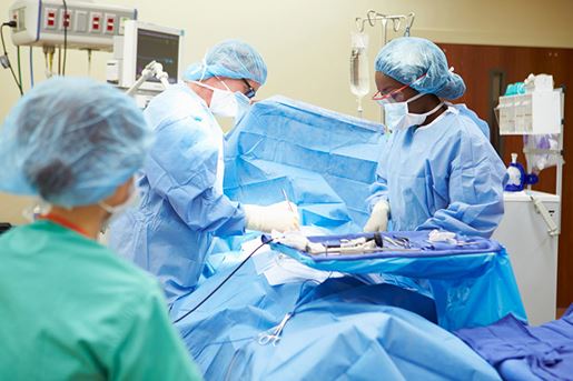 Surgical Team Working In Operating Theatre Wearing Protective Clothing