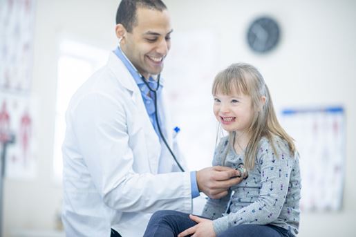young girl with Down Syndrome sitting patiently while having her heart checked by doctor